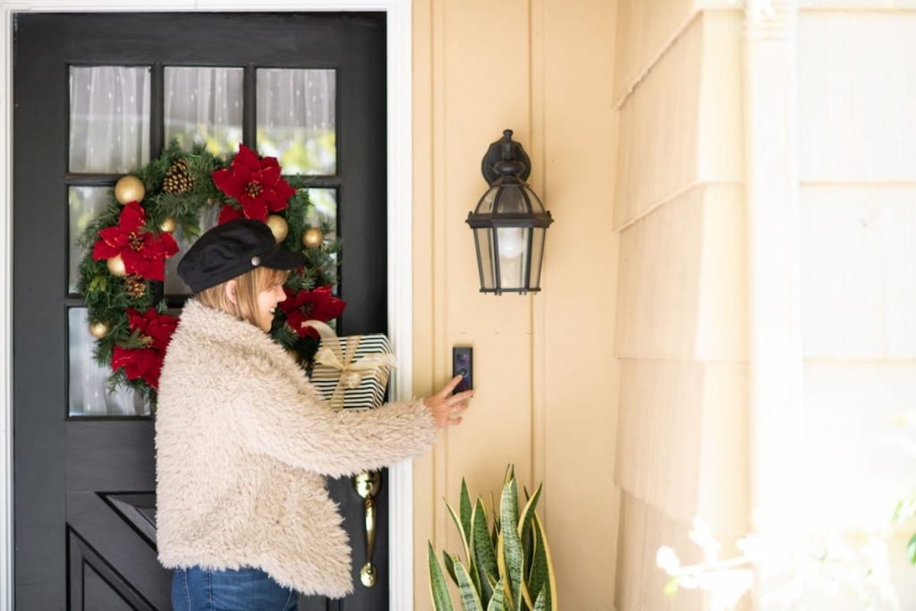 poinsettia wreath at front door with a woman ringing the door bell